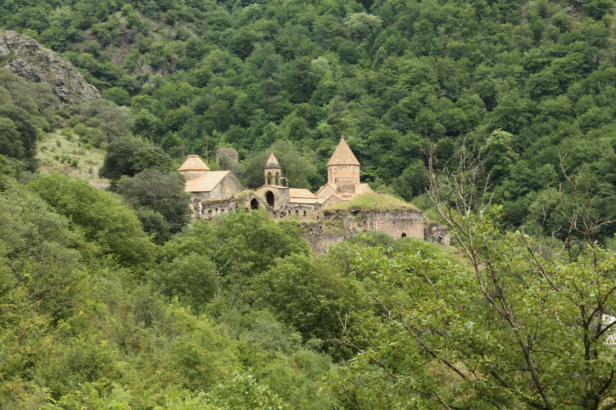 Cluster of stone monastery churches and halls with red tiled roofs on a green mountain slope