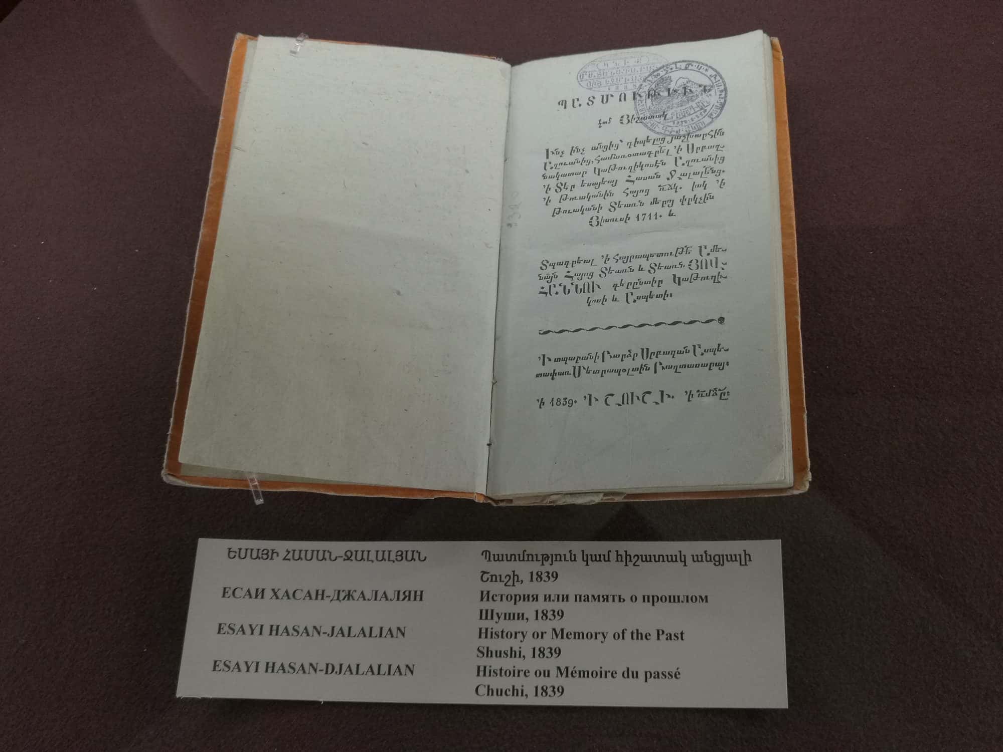 Old printed book open in a museum display case with Armenian text on both pages
