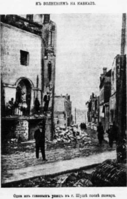 Black and white newspaper photograph of a burned out street of houses, roofless walls and rubble