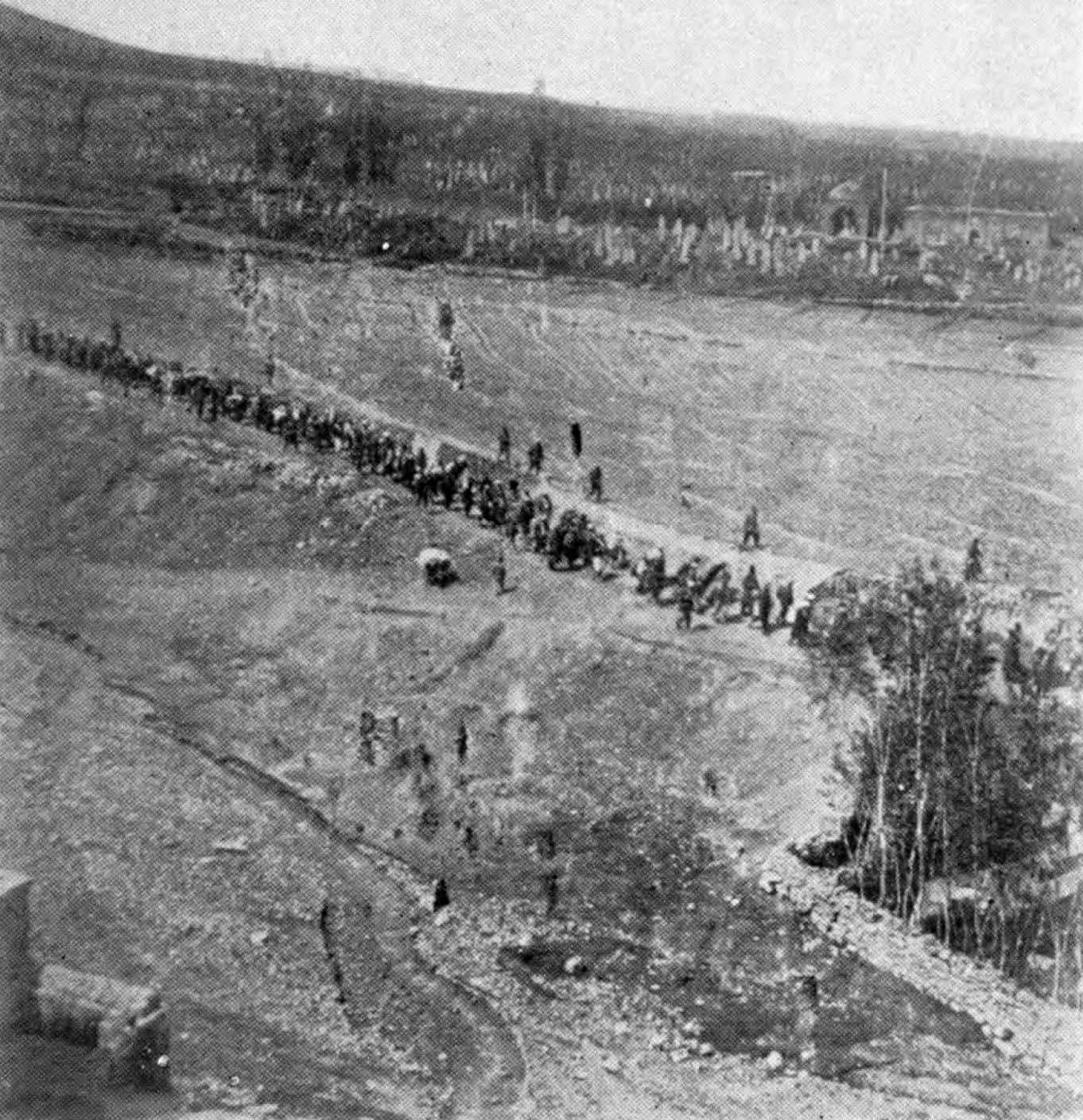 Long column of people walking away from the camera along a dirt track across open country