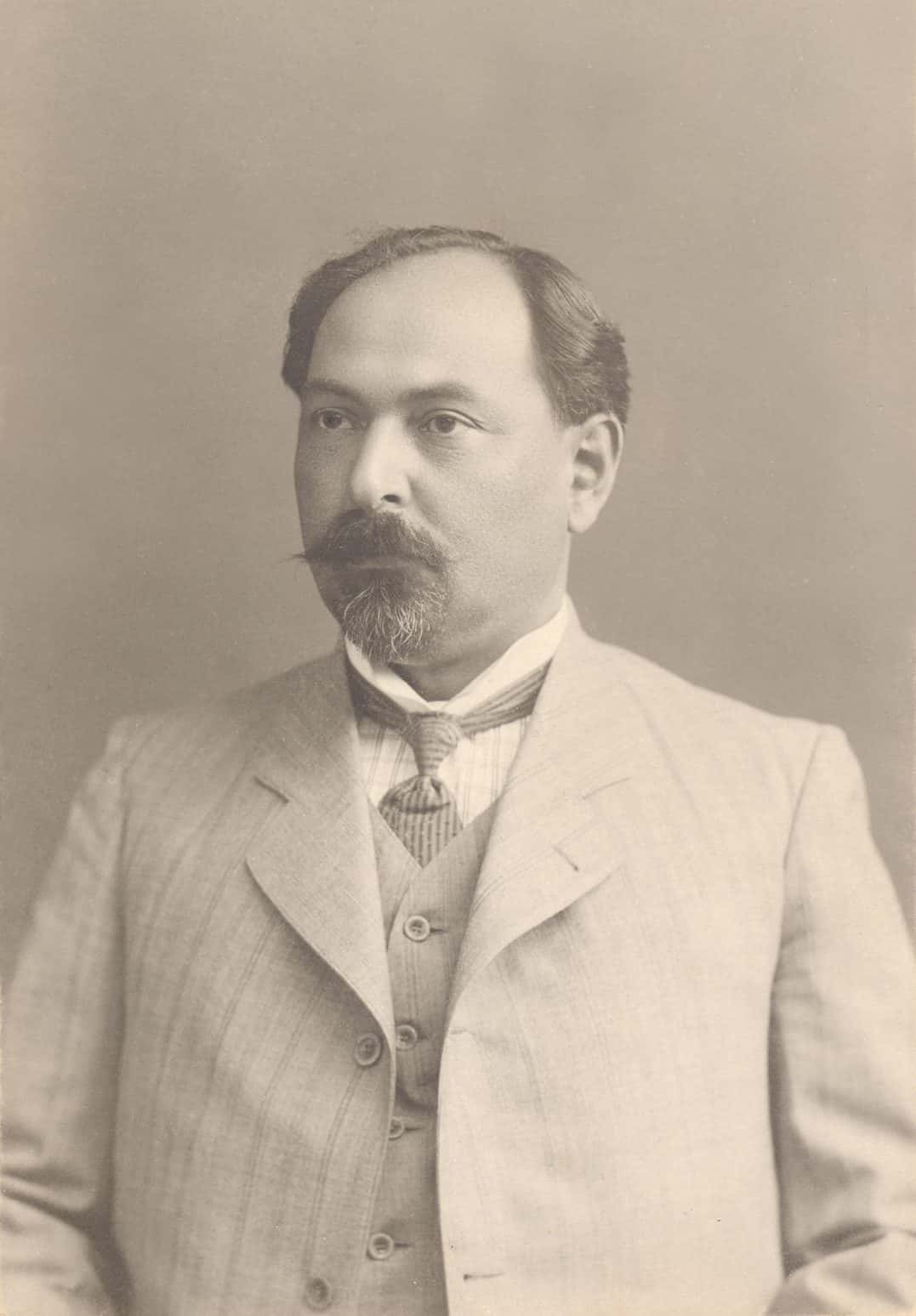 Formal studio portrait of a seated man in a dark suit and tie
