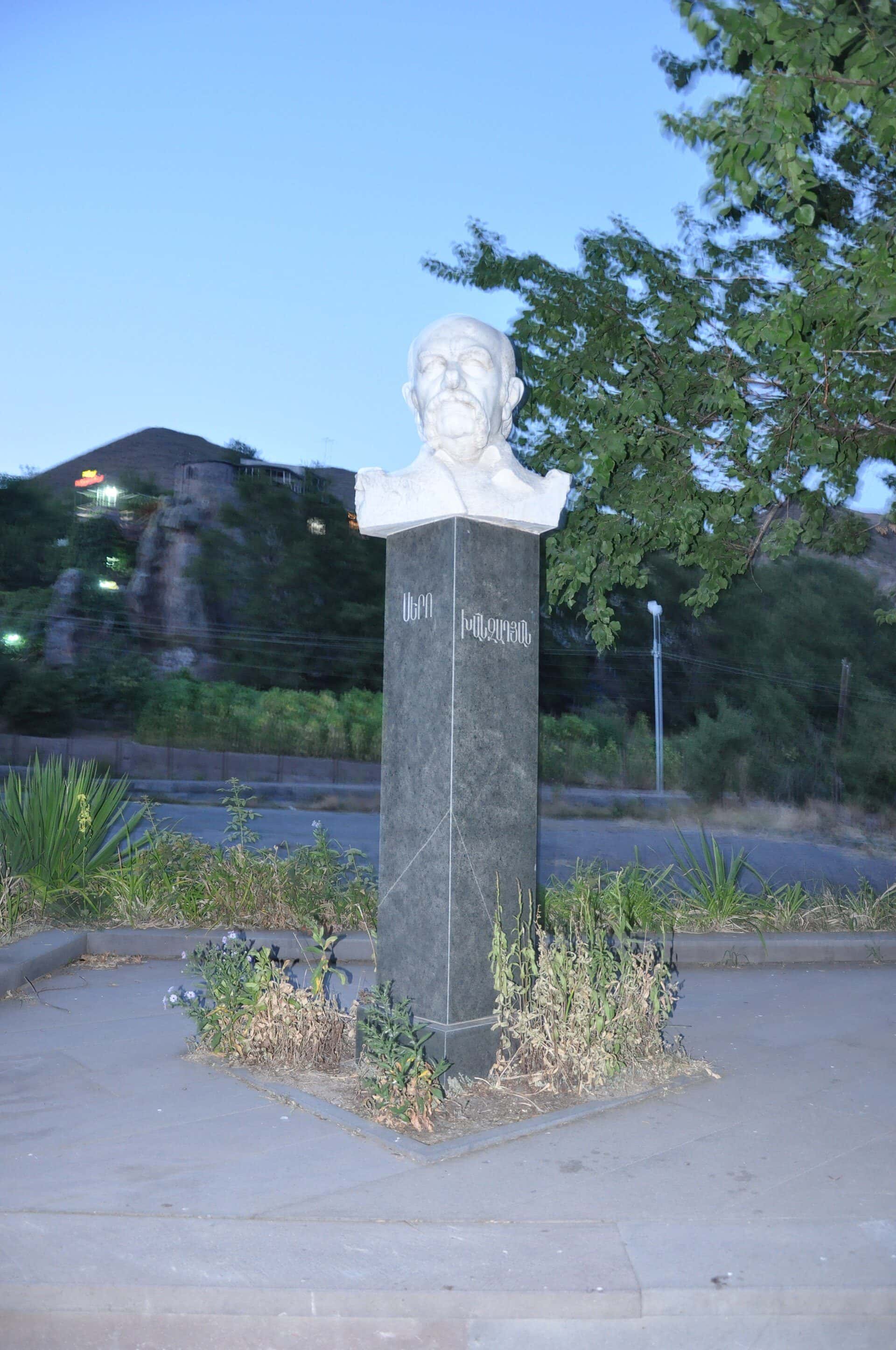 Bronze bust of a man on a stone plinth, trees behind