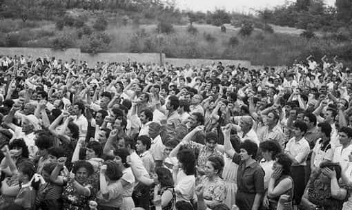 Black and white photograph of a dense outdoor crowd, many hands raised above their heads