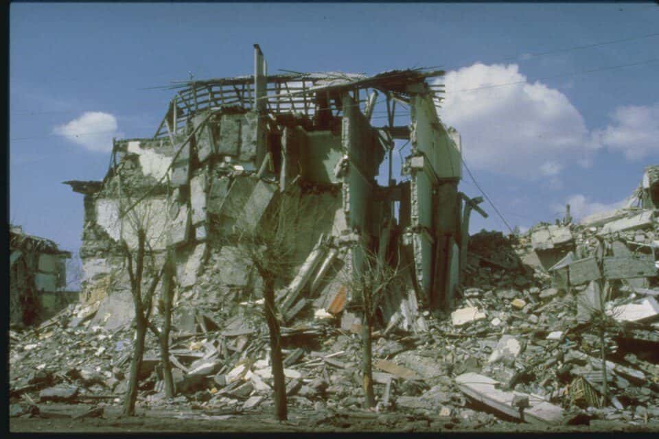 Colour photograph of a multi storey building whose floors have pancaked onto one another, rubble below