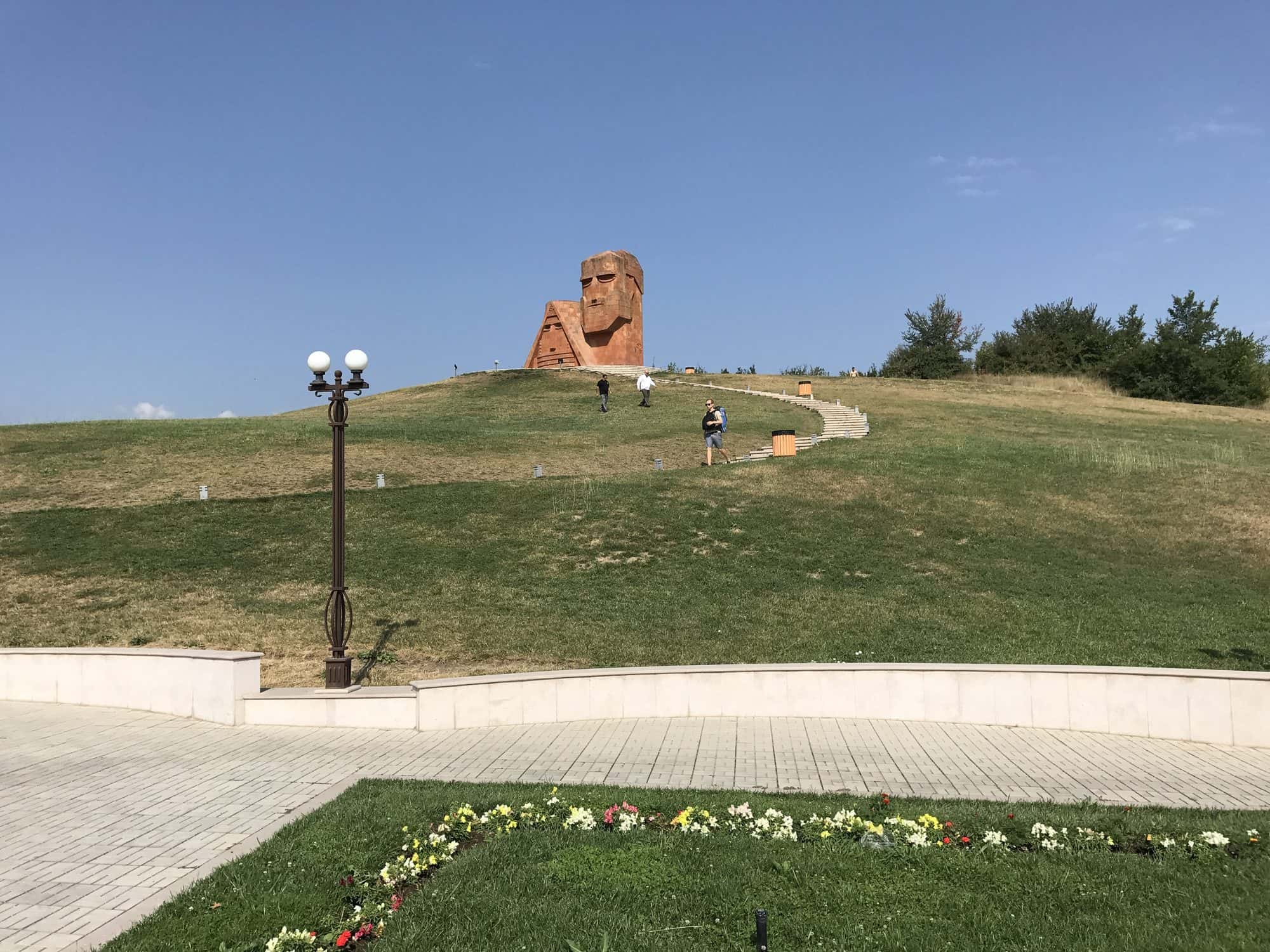Large tufa sculpture of an elderly man and woman carved from rock, standing on a hillside near Stepanakert