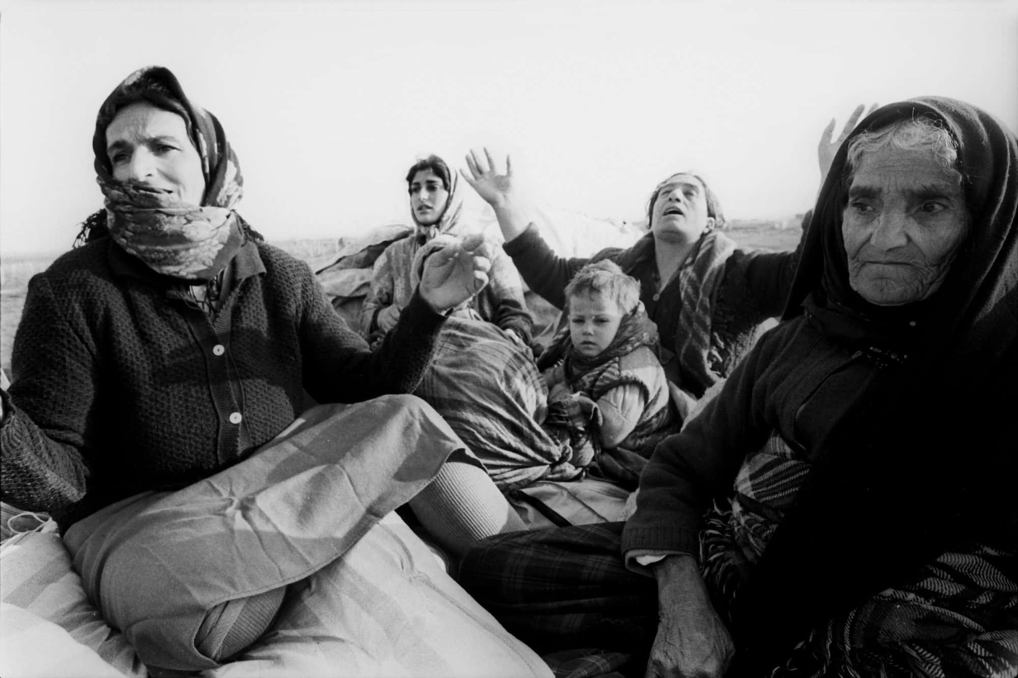 Black and white photograph of women and small children sitting with bundles of belongings after fleeing their town