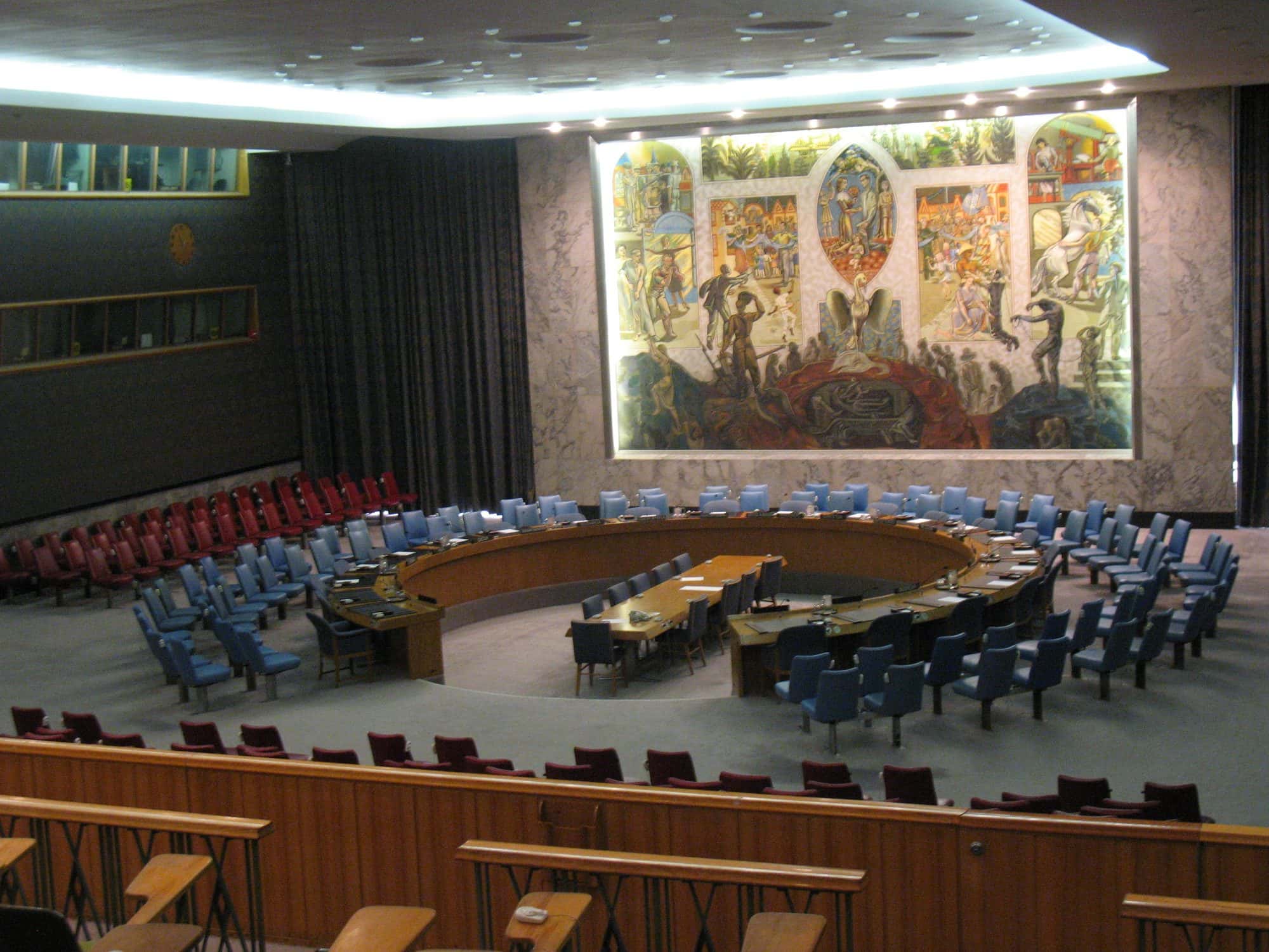 Delegates seated around the horseshoe table of the United Nations Security Council beneath its mural