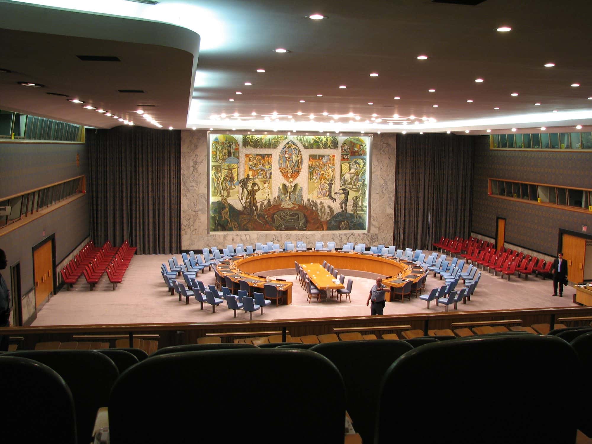 Wide interior view of the United Nations Security Council chamber with its circular table and mural