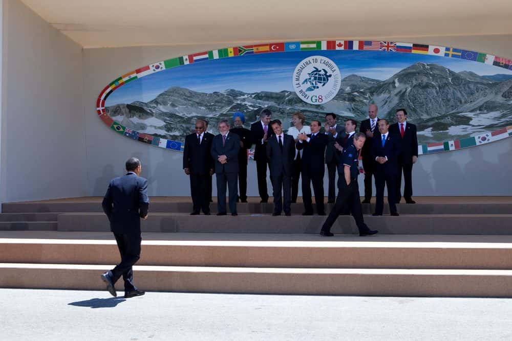 Barack Obama in a dark suit walking quickly toward a group of world leaders assembling outdoors