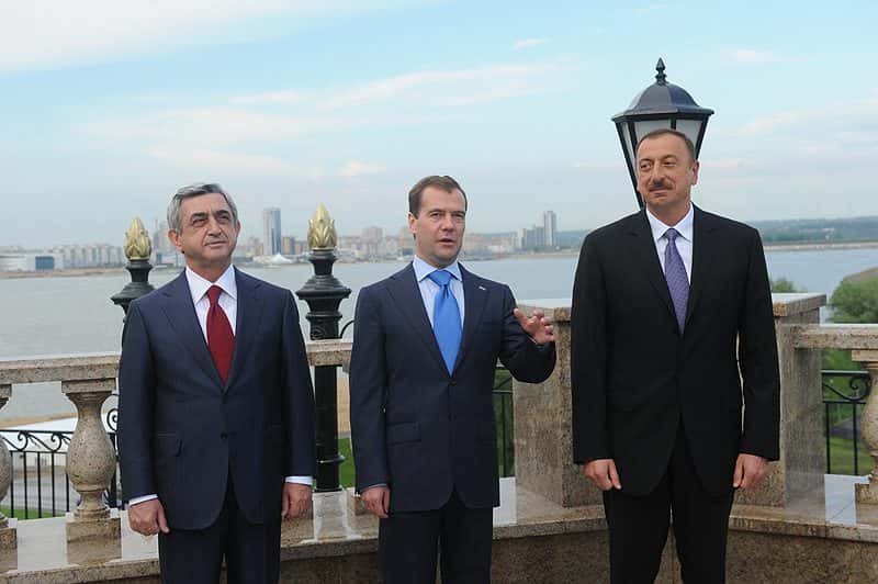 Three men in suits standing together in a hall before the start of a summit meeting