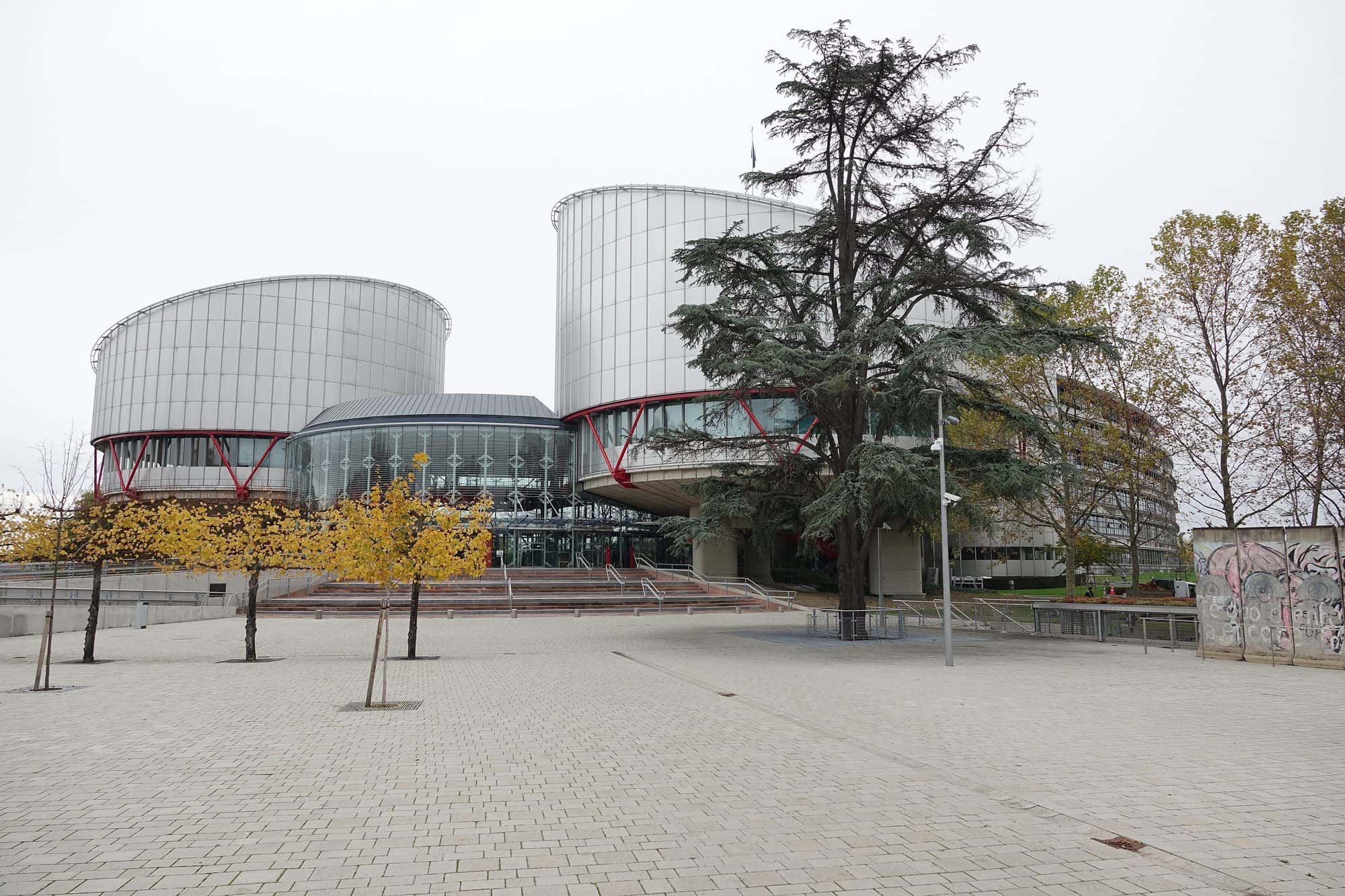 Curved glass and steel court building beside a river, with two cylindrical towers