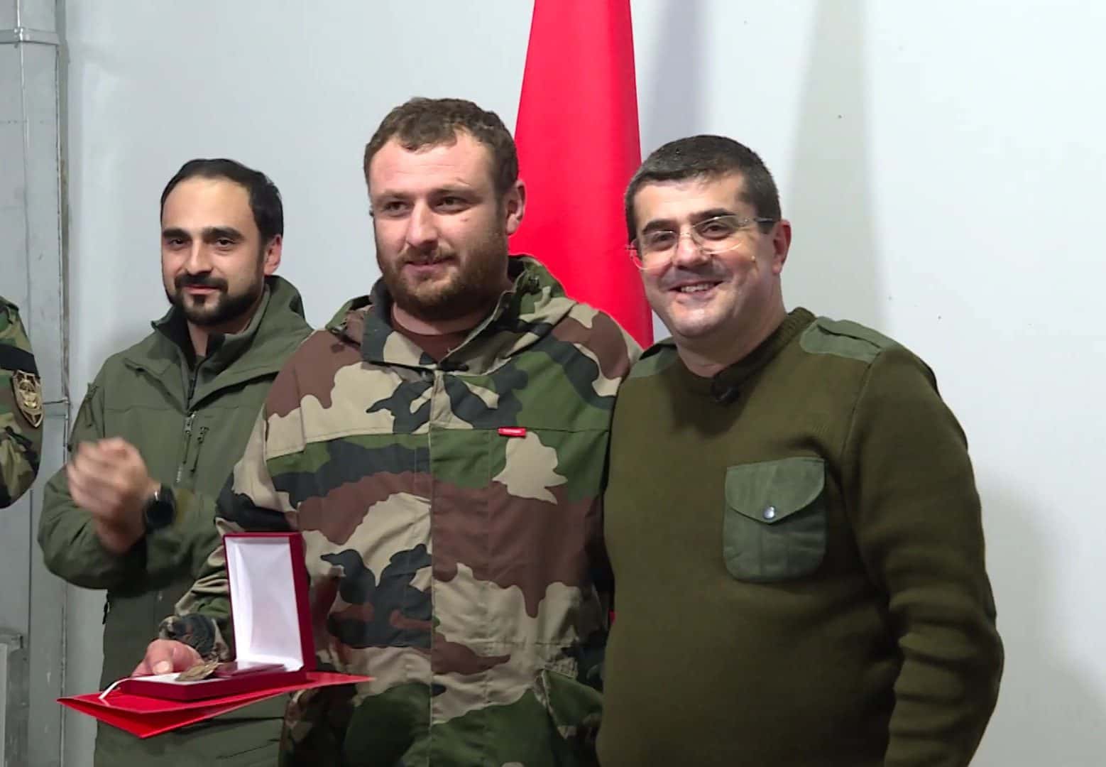 Arayik Harutyunyan in olive fatigues and glasses standing beside a decorated volunteer