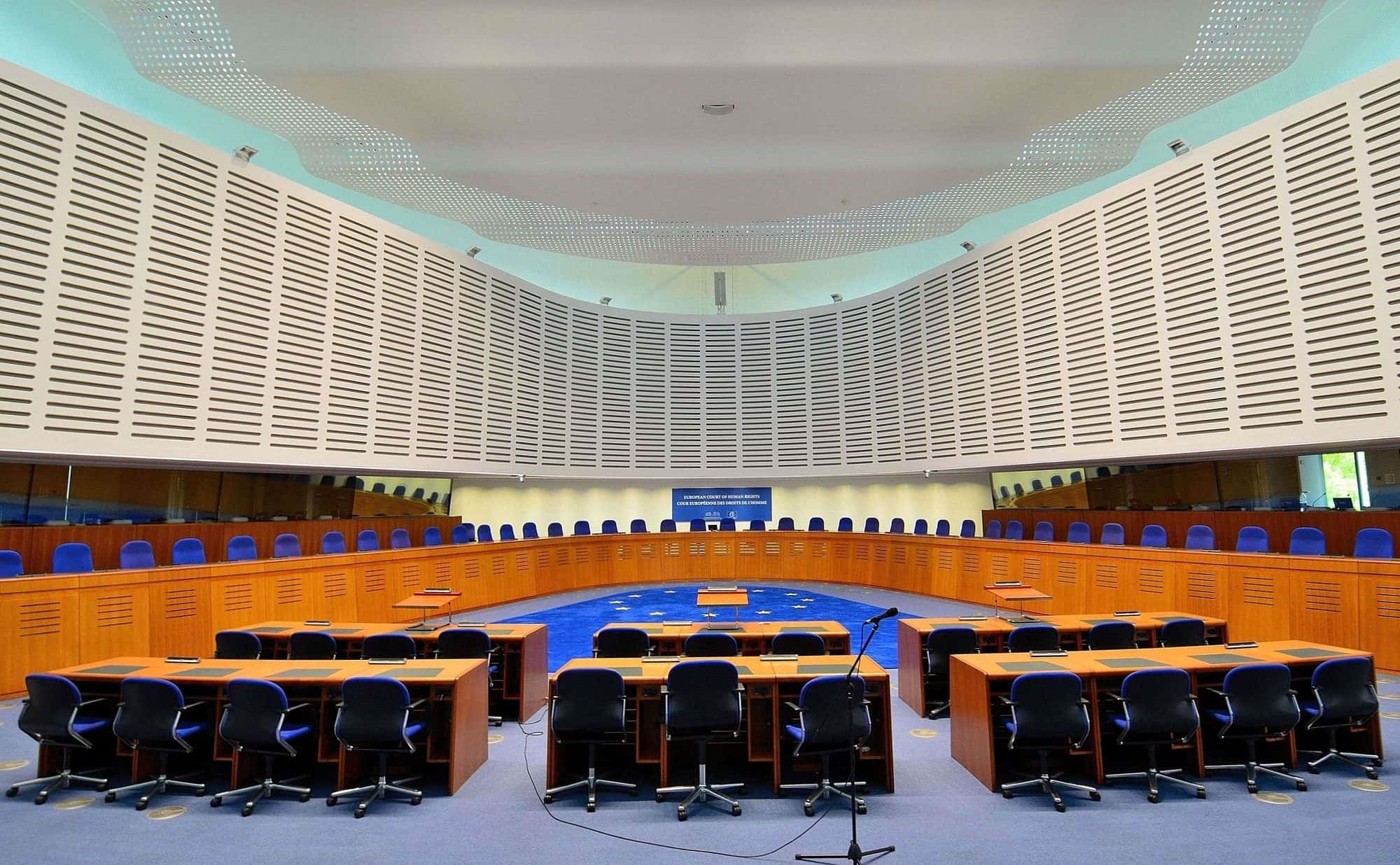 Empty modern circular courtroom with wooden benches and the court's emblem on the wall