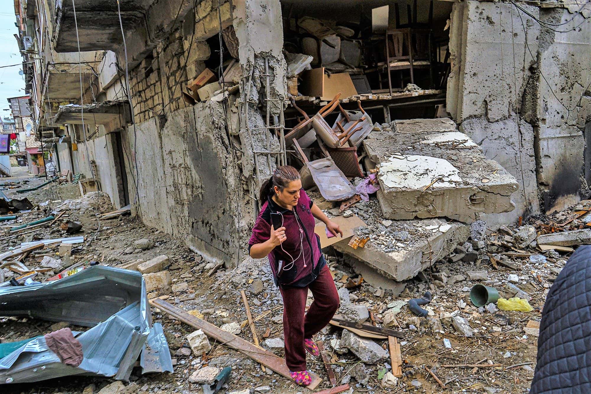 Woman walking through debris past a shell damaged apartment block with collapsed walls and exposed rooms