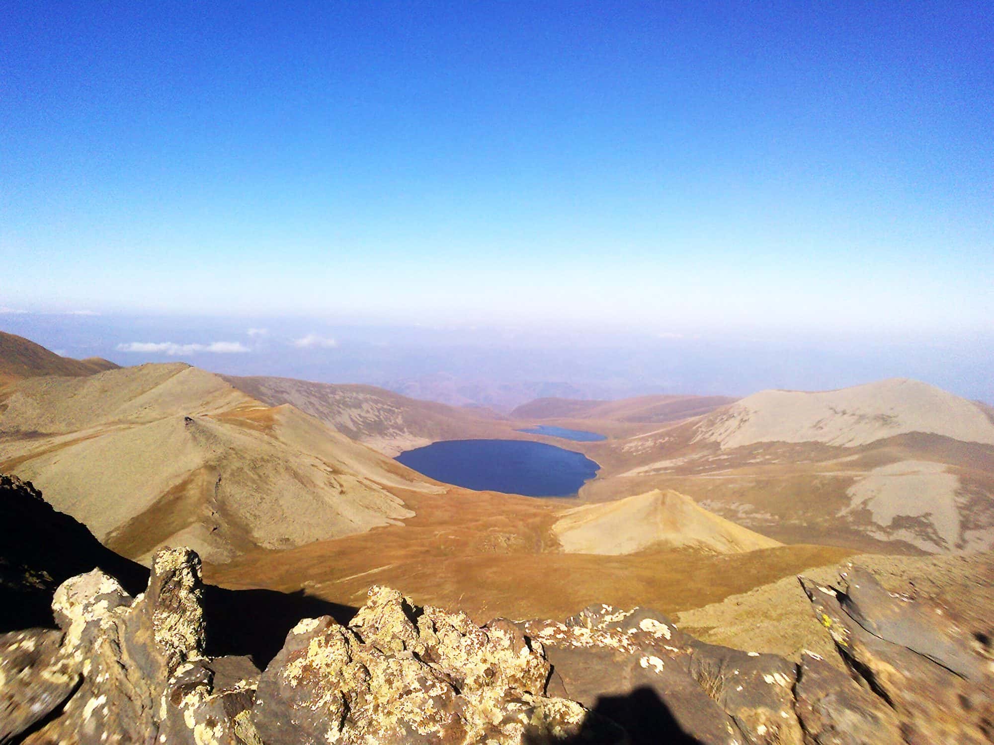 High altitude lake ringed by bare grassy mountain slopes under a clear sky