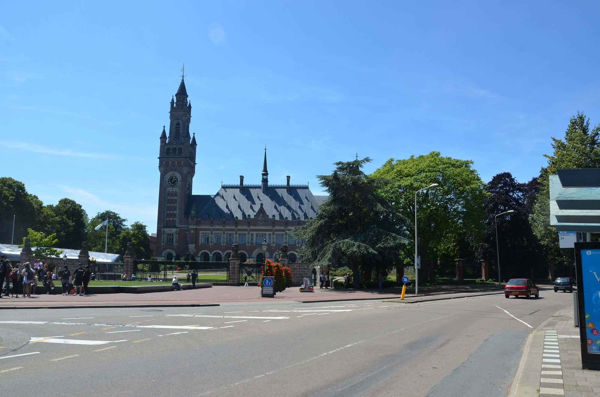 Red brick palace with a tall clock tower seen across its forecourt