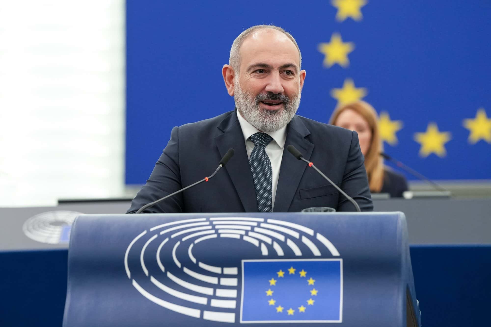 Nikol Pashinyan standing at a lectern speaking, microphones in front of him