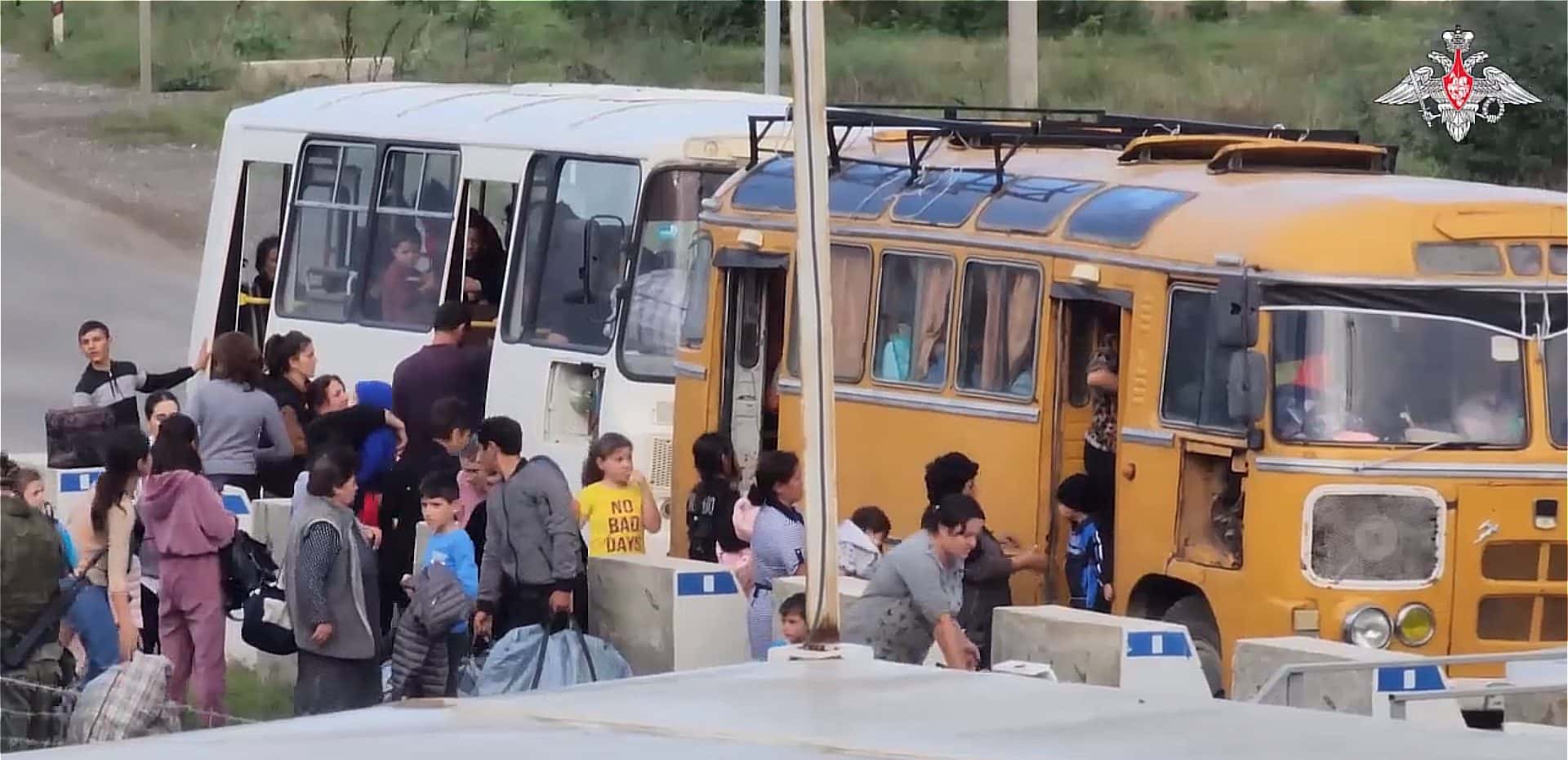 Civilians with bags boarding two buses on a roadside, children and adults queuing