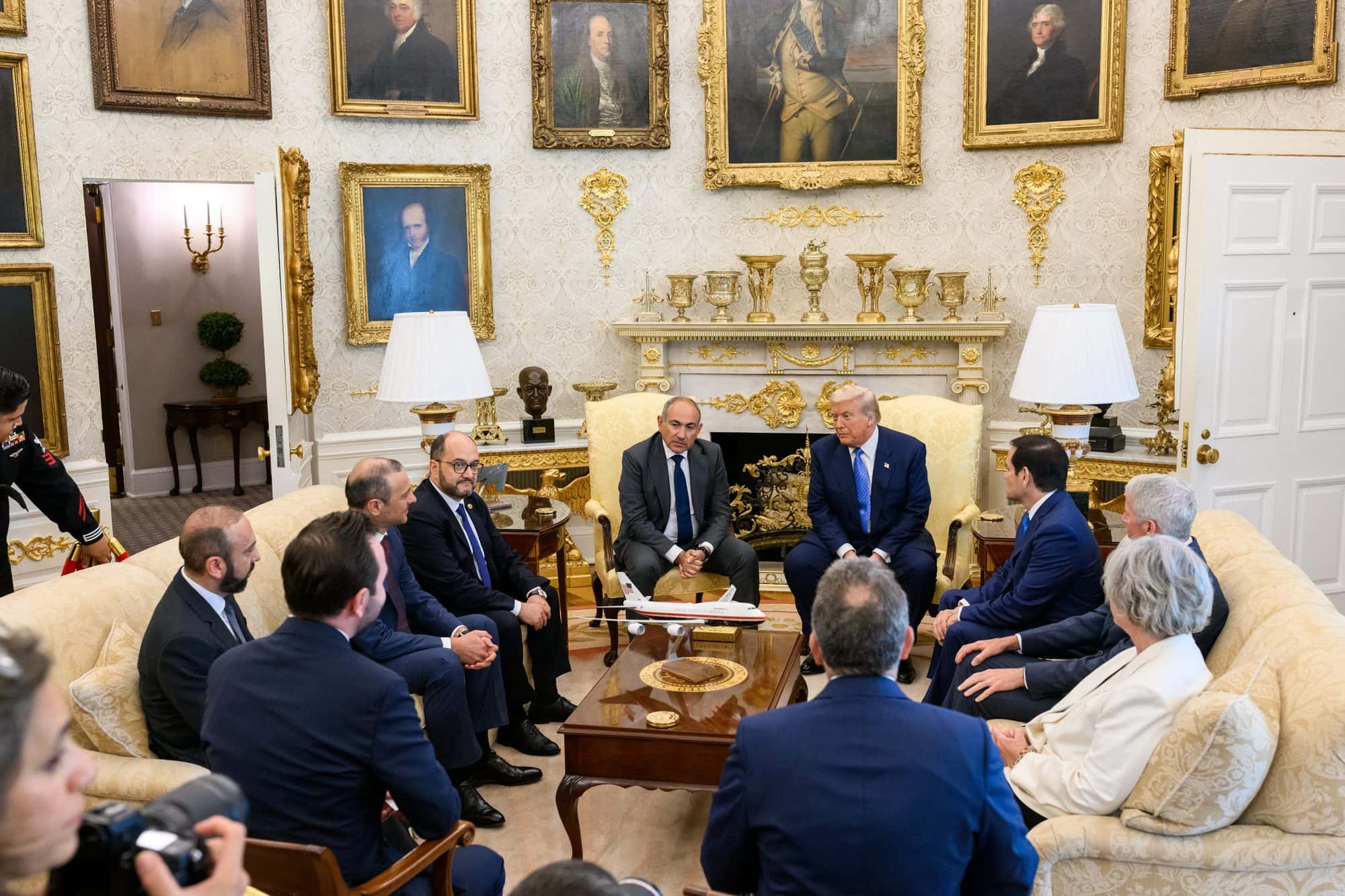 Three leaders seated at a table signing documents in a White House room