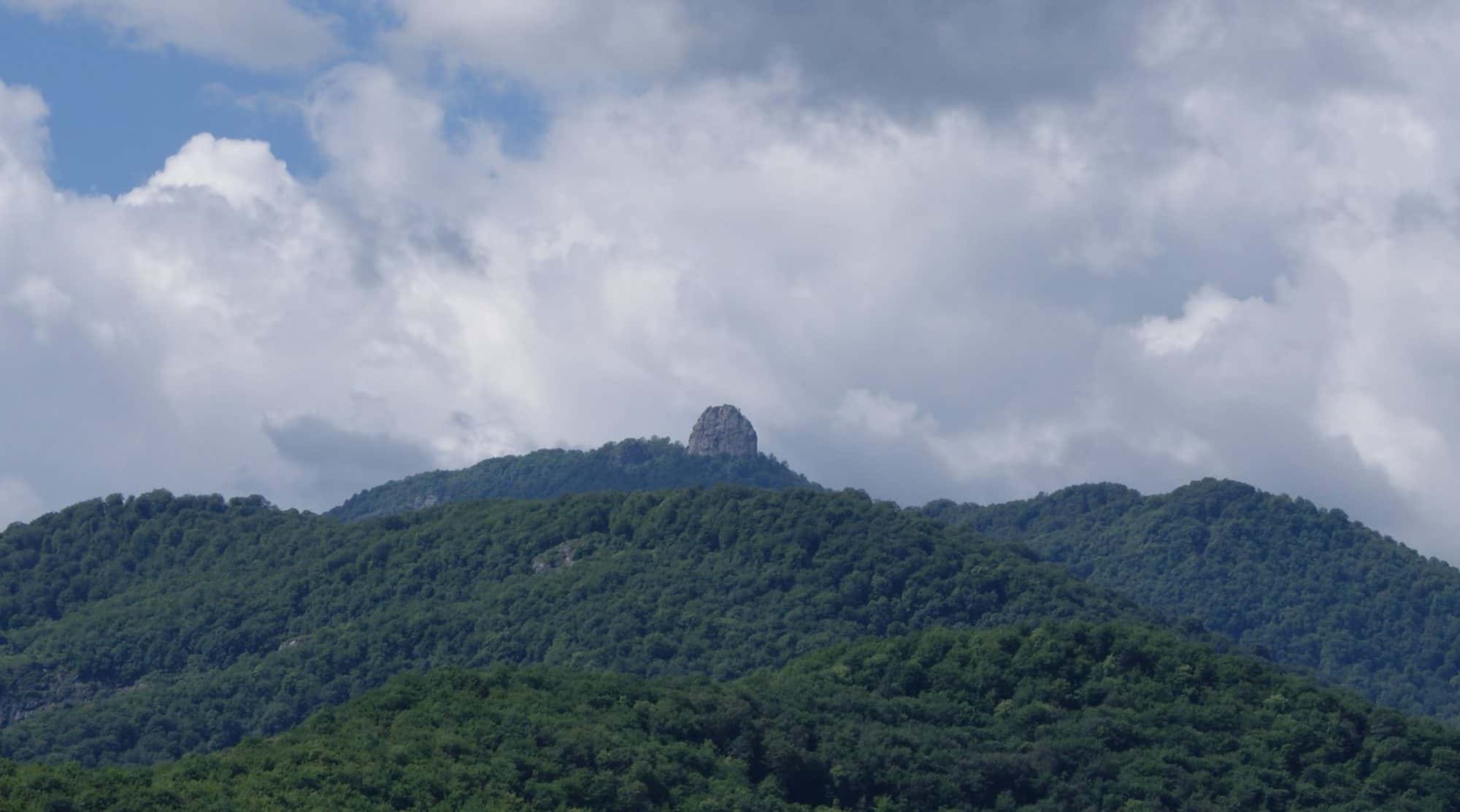 Ruined stone fortress walls on a high rocky outcrop above wooded mountain slopes