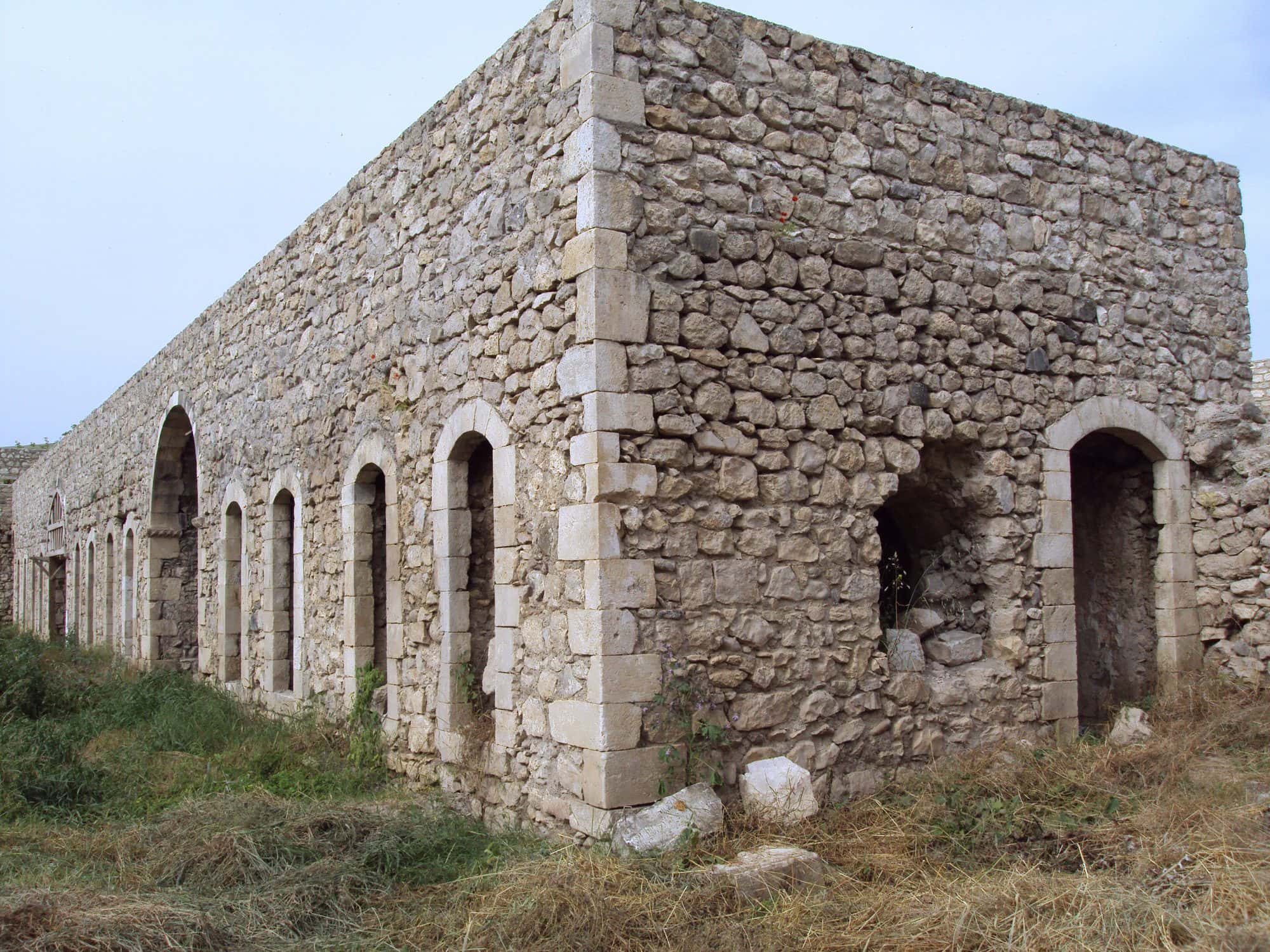 Stone monastery church inside a rectangular fortified wall, green hills and open sky behind