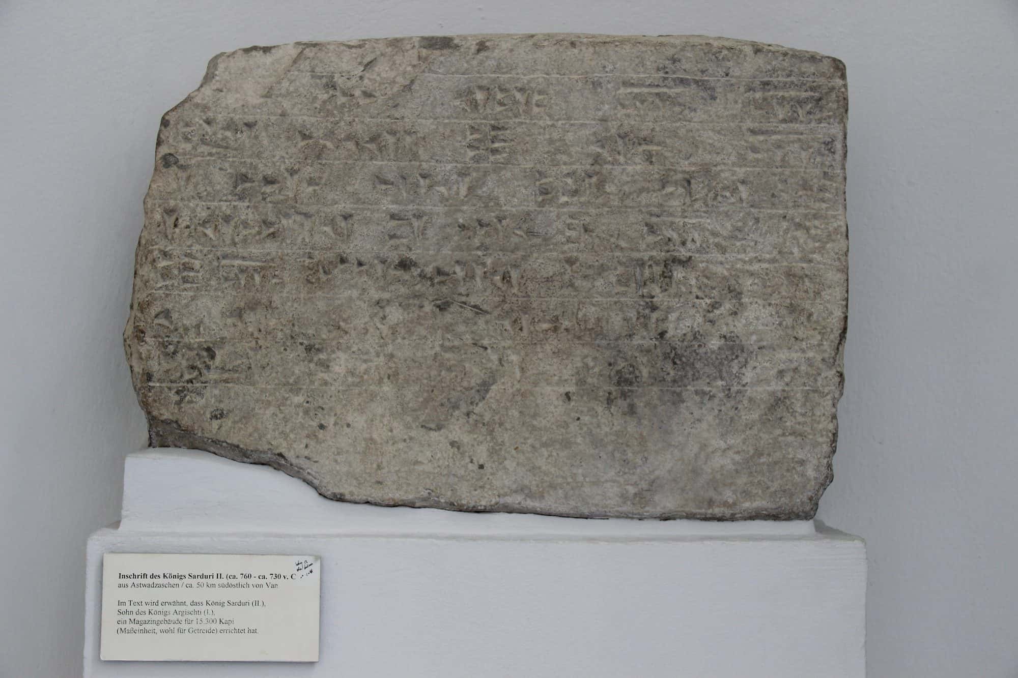 Weathered basalt block carved with dense rows of Urartian cuneiform wedge signs, museum display
